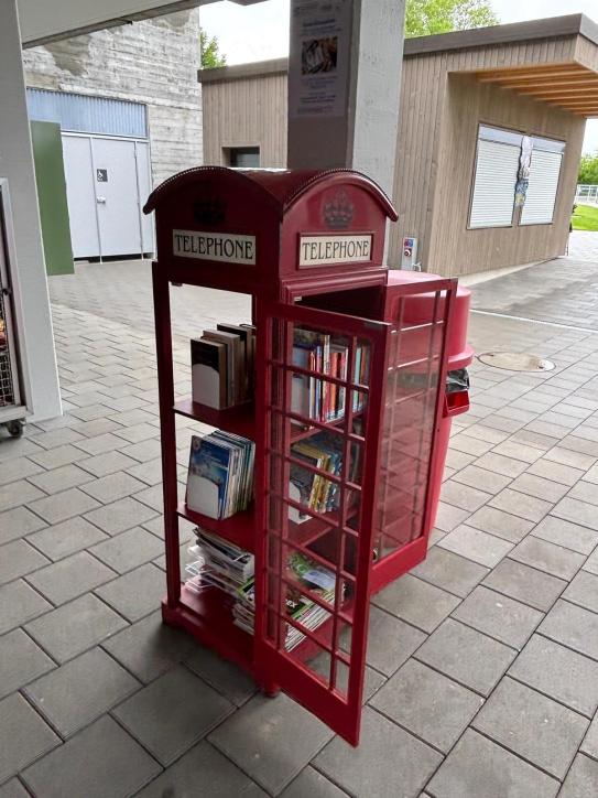 Bild von roter Telefonkabine im Stil der Telefonkabinen aus Englad. In der Telefonkabine werden Bücher und Magazine ausgestellt, welche von den Gäste während ihres Aufenthalts im Freibad Hirzi kostenlos ausgeliehen werden können.